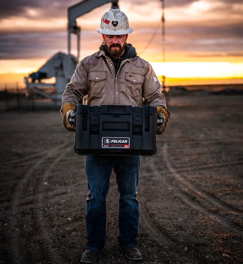 Worker carrying a Pelican CRATE case in an oil field